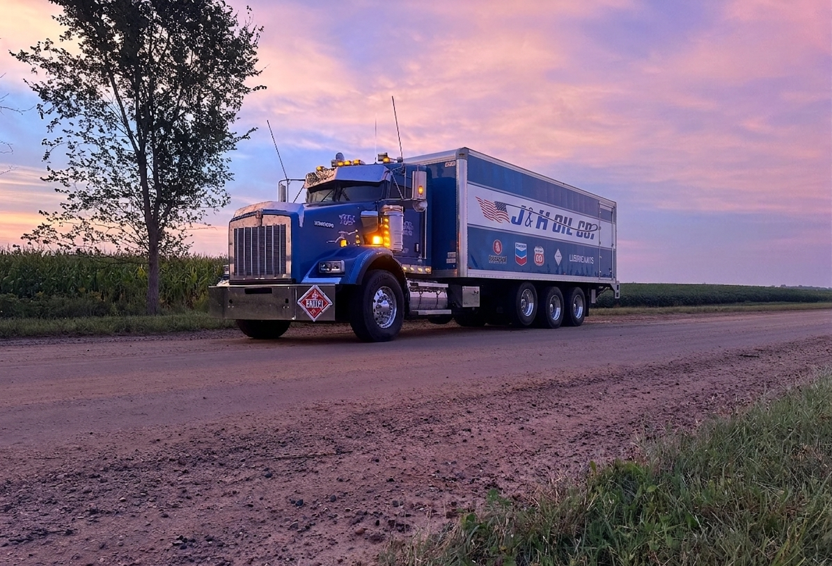 J & H Oil Company lubricants delivery truck on a dirt road beside a cornfield